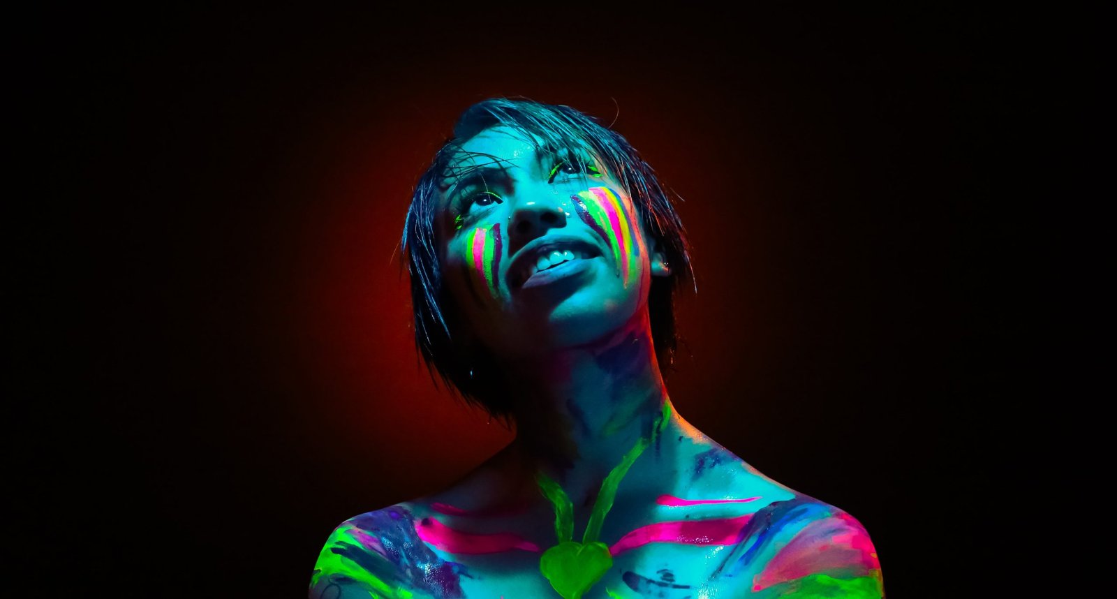 Mulher negra olhando para cima e com o corpo pintado com tinta colorida