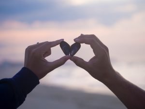A mão de um homem e de uma mulher juntando cada um a metade de uma pedra e formando um coração