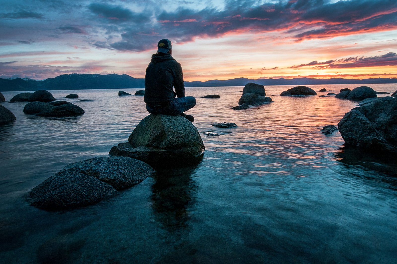 Homem sentando em uma pedra e admirando o mar