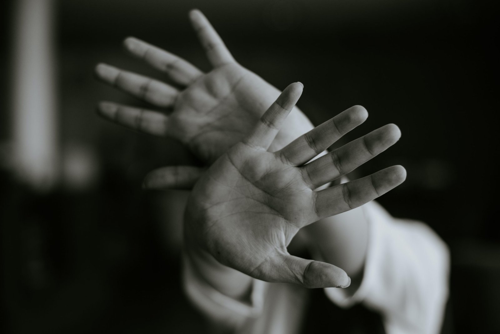 Foto em preto e branco de um homem colocando as mãos em direção ao observador, como se estivesse negando algo