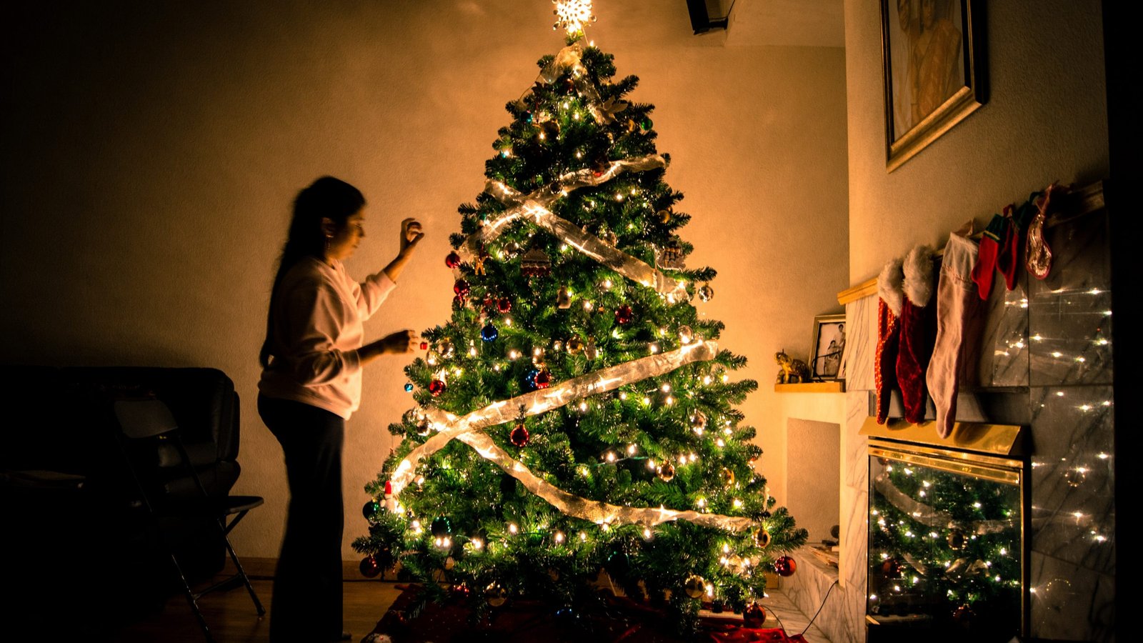 mulher decorando uma grande árvore de natal na sala de casa