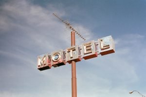 Placa de um motel afixada em uma barra de cano marrom e com uma antena de tv no topo