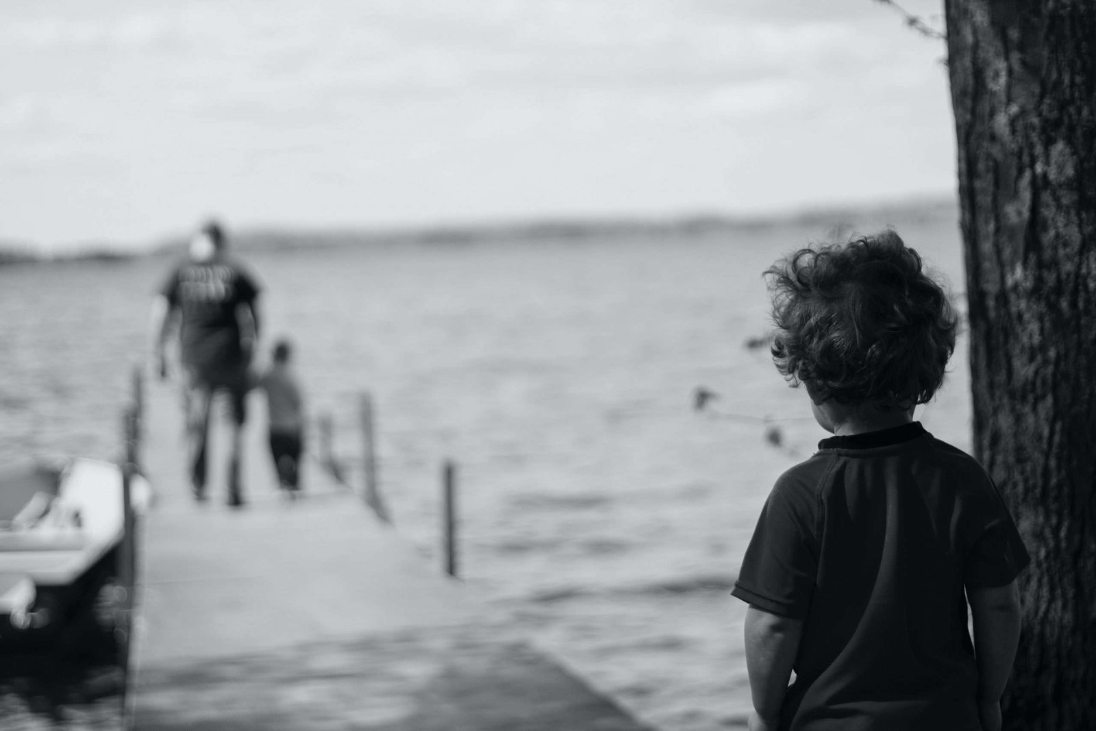 Foto em preto e branco de um garoto olhando seu pai de mãos dadas com o irmão em cima de um trapiche de madeira