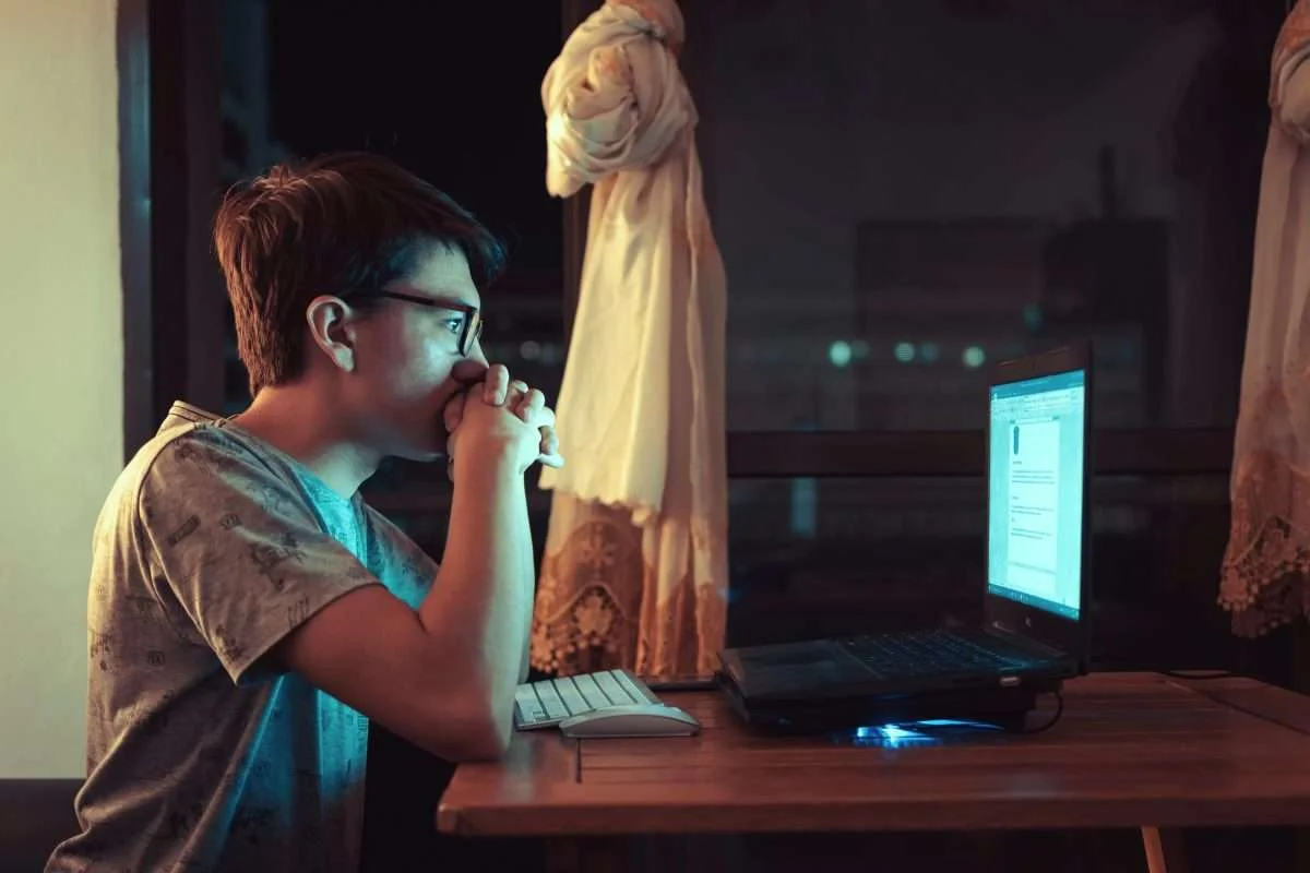 Mulher de óculos e cabelos cursos olhando a tela de um notebook durante a noite