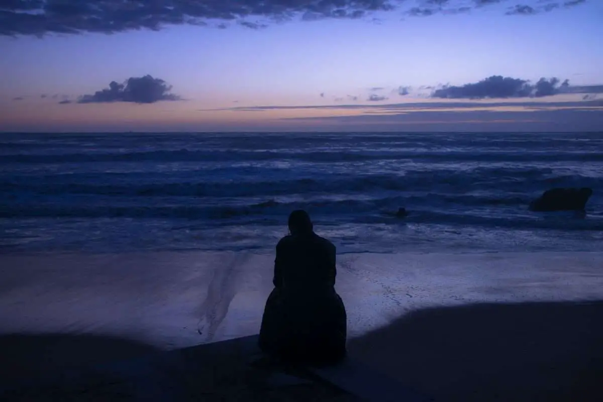 Homem sentado na praia à beira do mar durante um crepúsculo