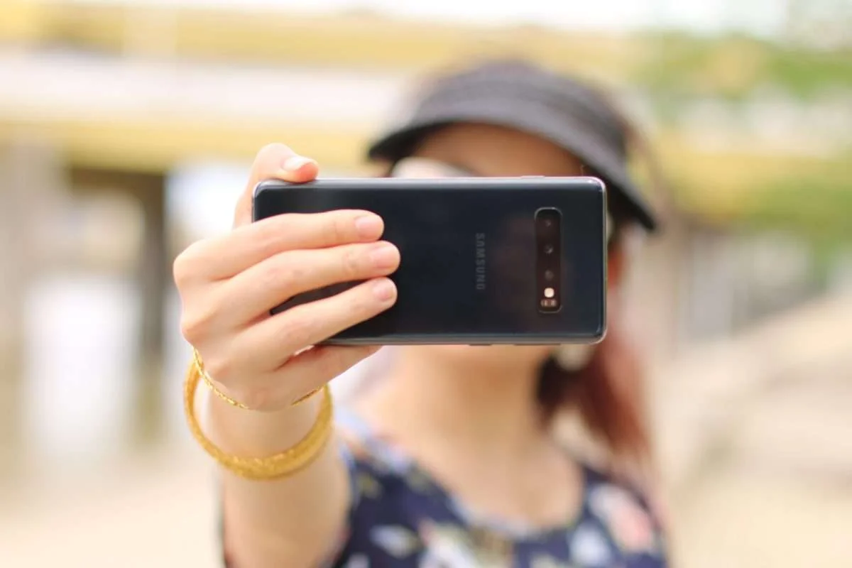 Mulher segurando um celular com a mão direita enquanto tira uma selfie