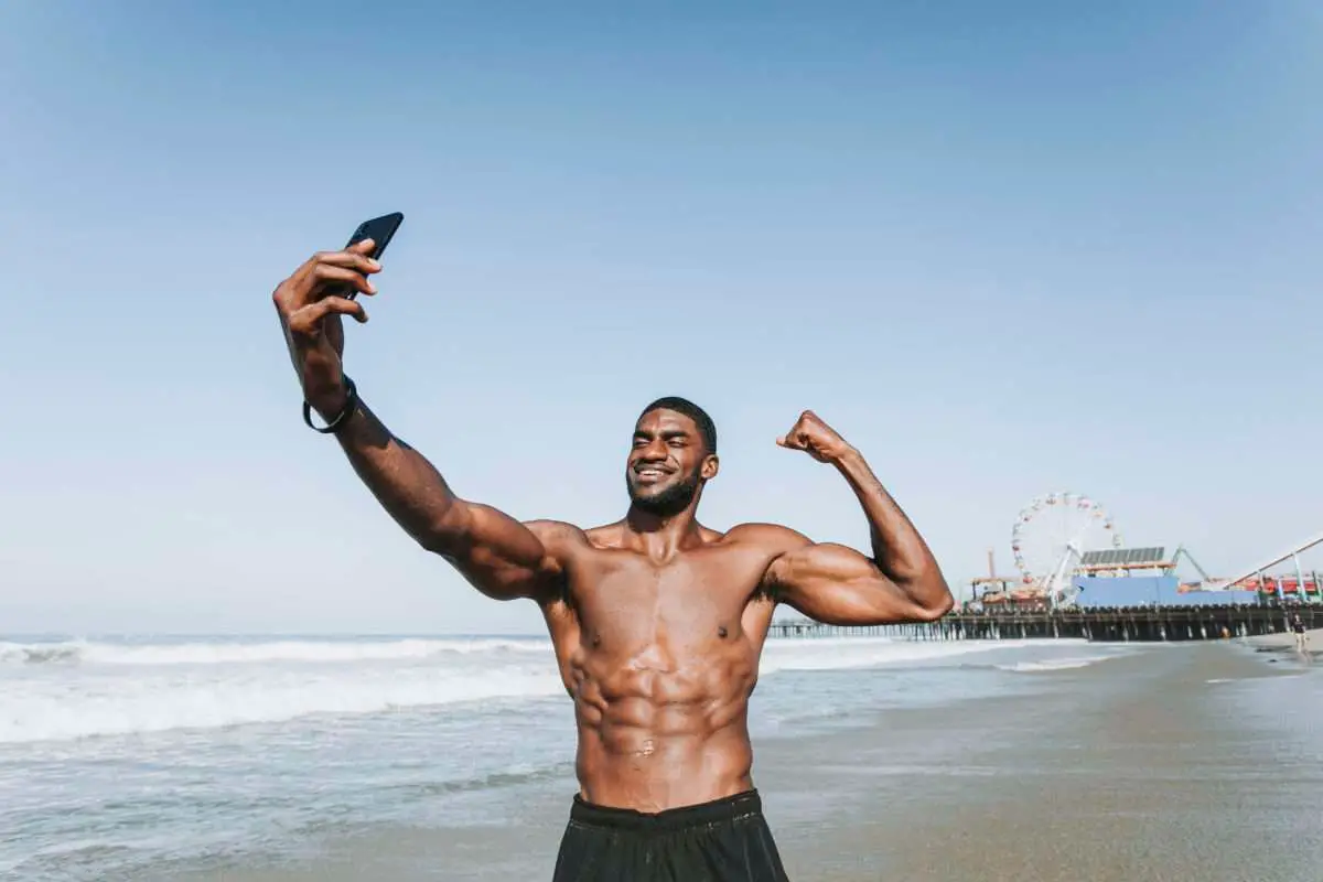 Homem negro e musculoso tirando uma selfie na praia