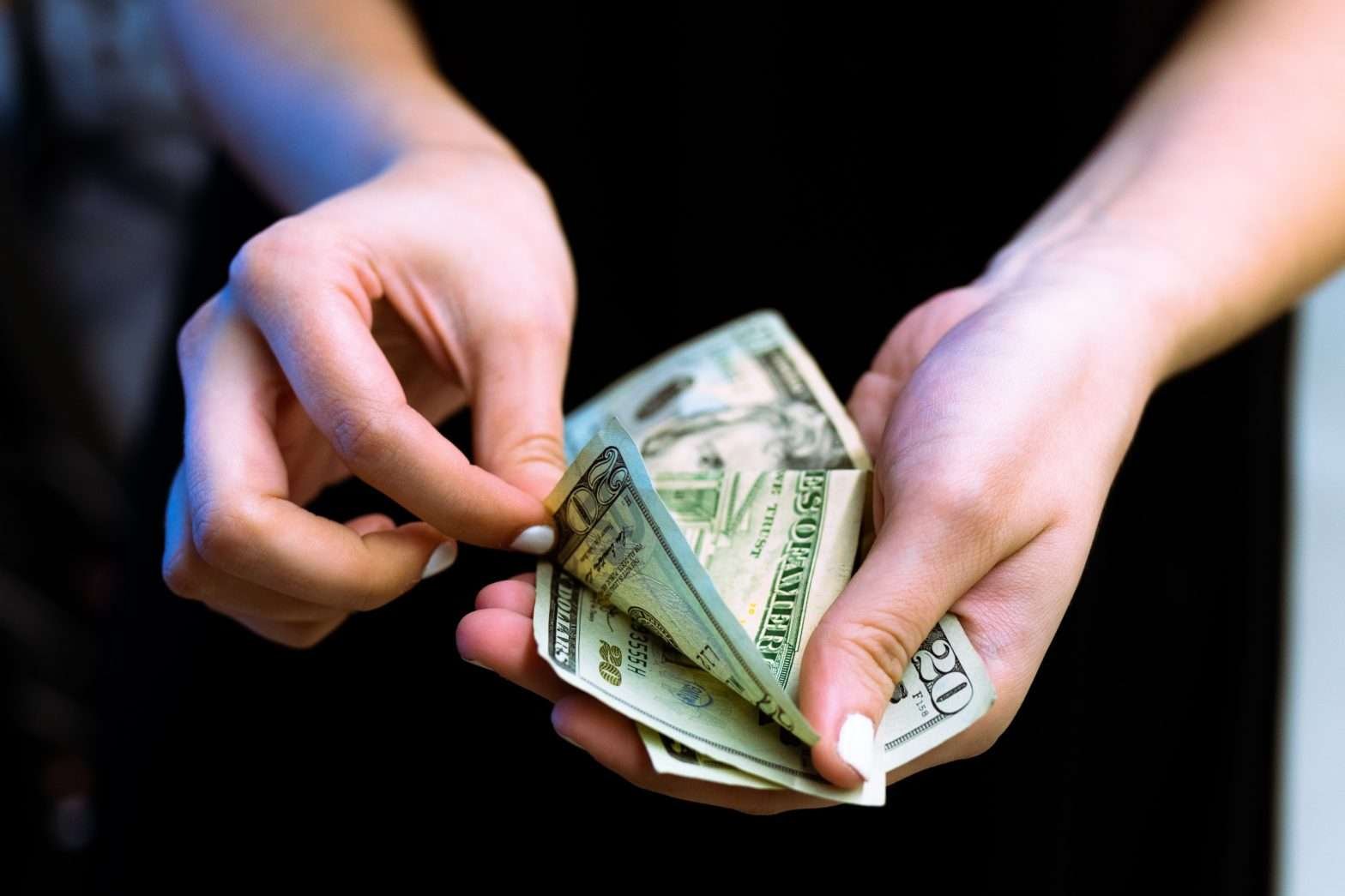 Mãos de mulher contando uma série de notas de 20 dólares