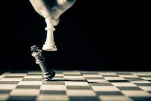 Uma mão segurando o rei branco do xadrez, enquanto derruba o rei preto