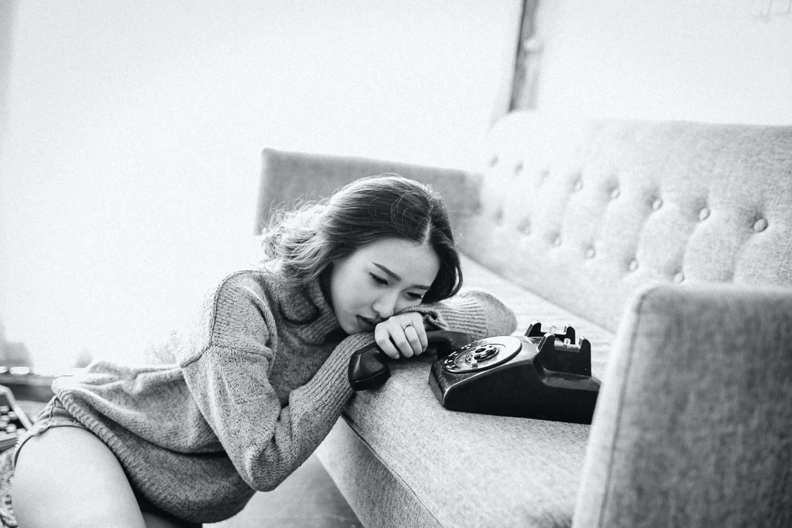 Imagem em preto e branco de uma mulher oriental apoiada em um sofá enquanto segura um telefone em sua mão esquerda