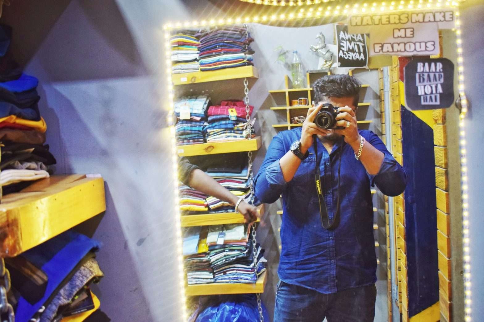 Homem de camisa azul fotografando a si diante do espelho