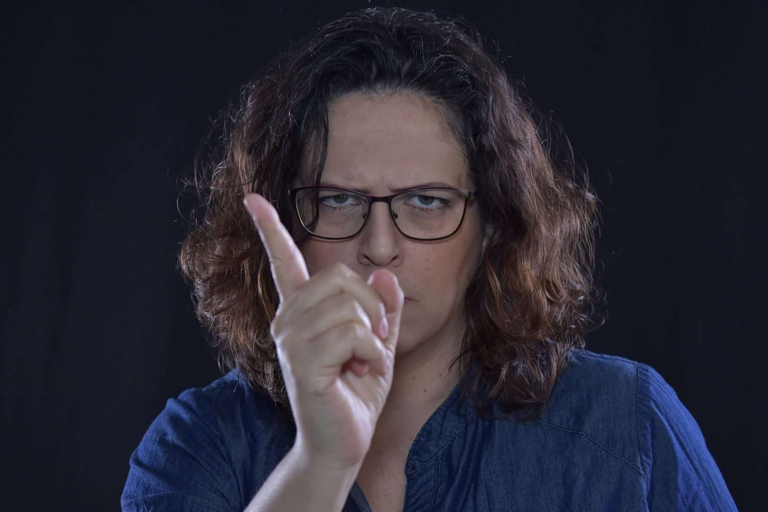 Mulher de óculos e camisa azul fazendo sinal de negativo com a mão