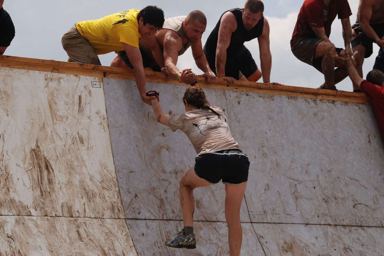 Homens no alto de um obstáculo ajudando uma mulher a subir