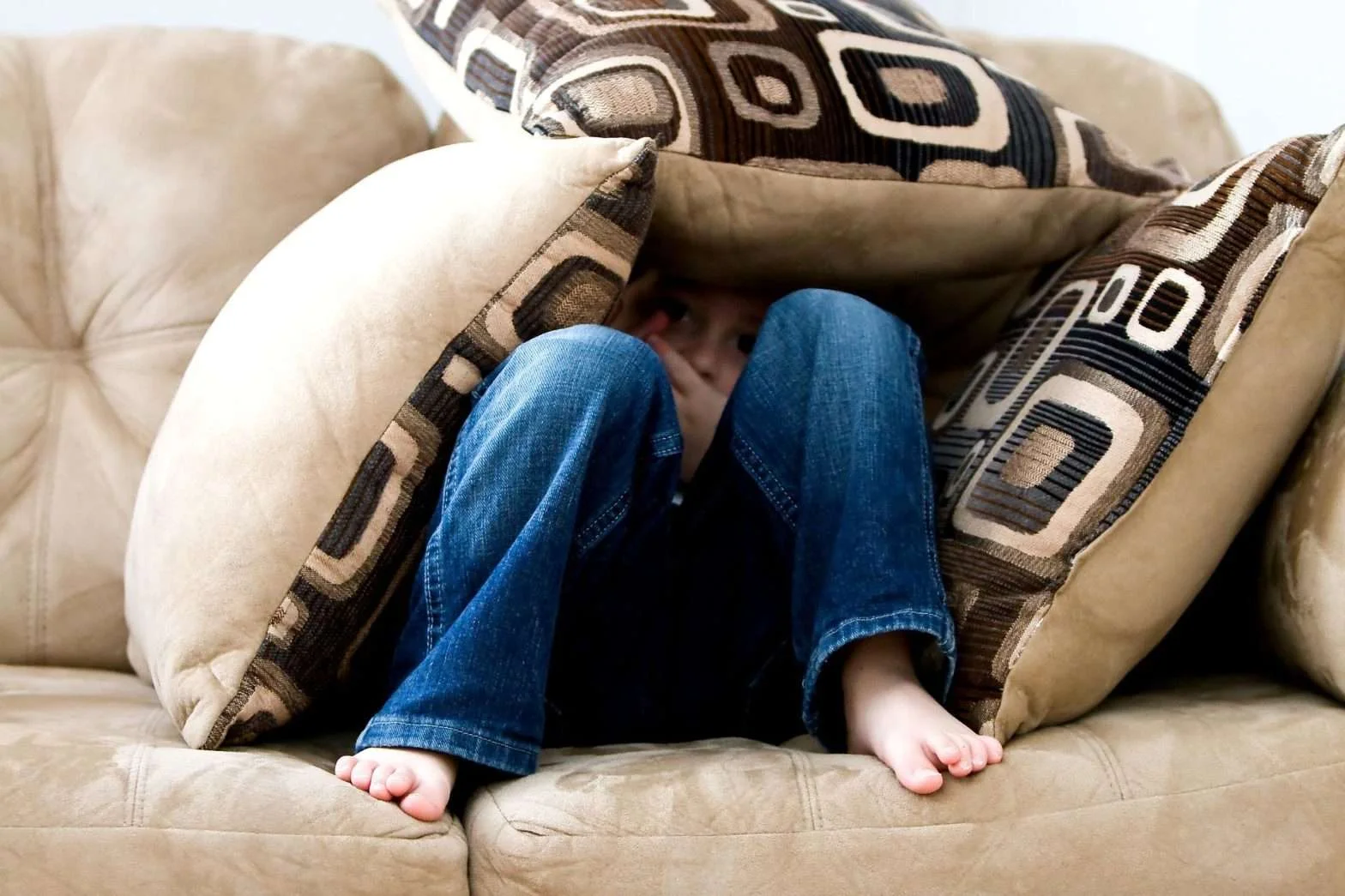 Homem escondido debaixo de várias almofadas em um sofá