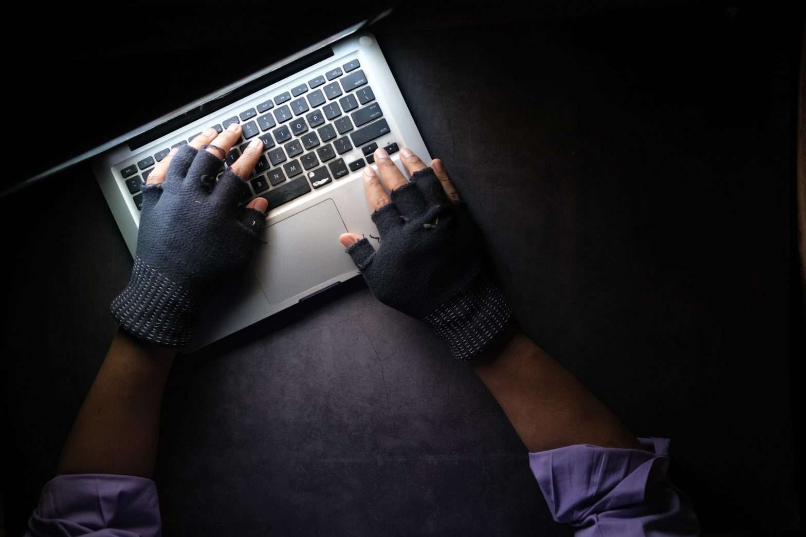 Homem com as mãos cobertas com luva em cima do teclado de um notebook