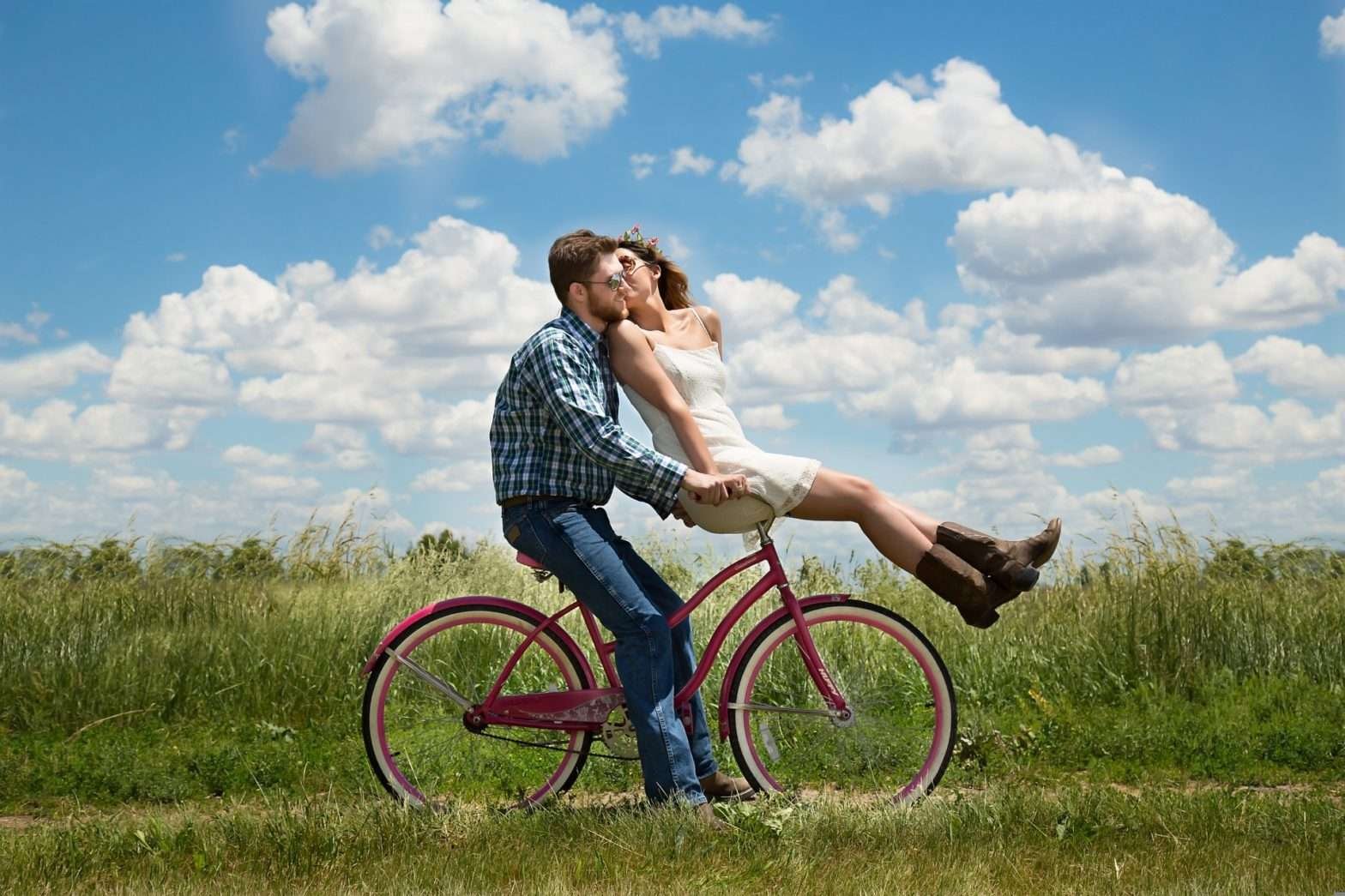 Casal andando de bicicleta enquanto a mulher dá um beijo no rosto do homem
