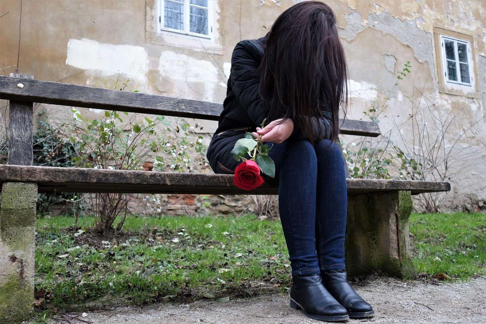 Mulher com a cabeça baixo sentada em um banco e segurando uma rosa vermelha