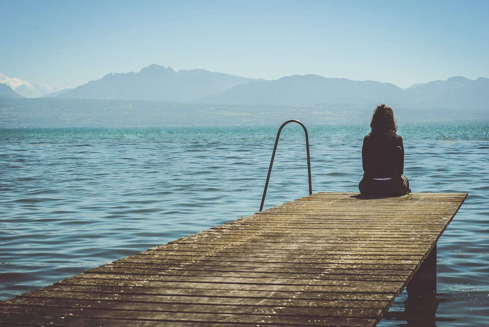 Mulher sozinha sentada na beira de um trapiche, de frente para o mar