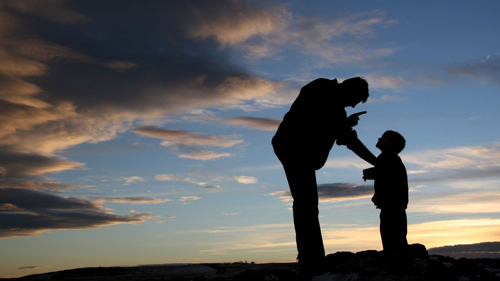 Silhueta de um homem apontando o dedo para seu filho durante o pôr-do-sol