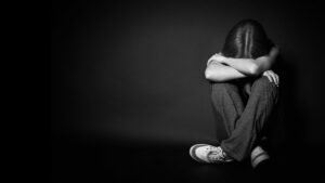 Foto em preto e branco de uma garota sentada de pernas cruzadas e escondendo o rosto em seus braços