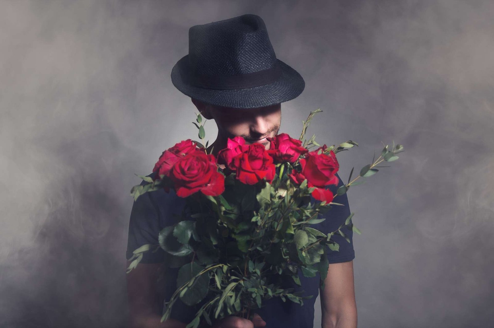 Homem com um chapéu preto segurando um buquê de rosas vermelhas