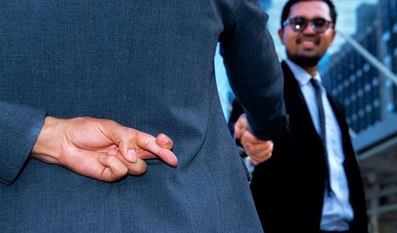 Pessoa cruzando os dedos enquanto aperta a mão de um homem de óculos