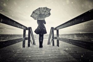 Mulher à beira da praia durante uma chuva e segurando um guarda-chuvas do avesso