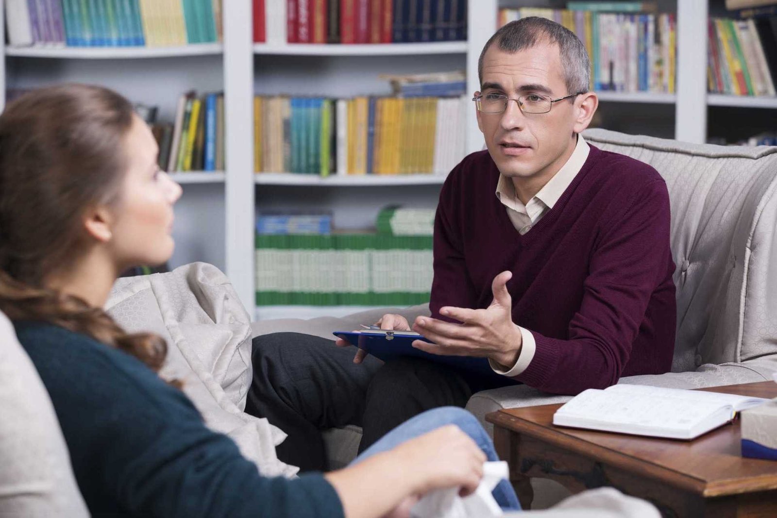 Uma mulher sentada em um sofá enquanto ouve um Psicólogo de óculos falando