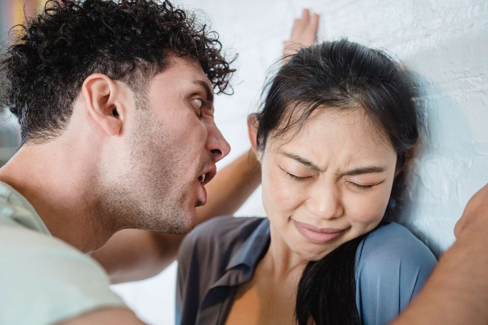Um homem cometendo abuso verbal contra uma mulher encostada na parede.