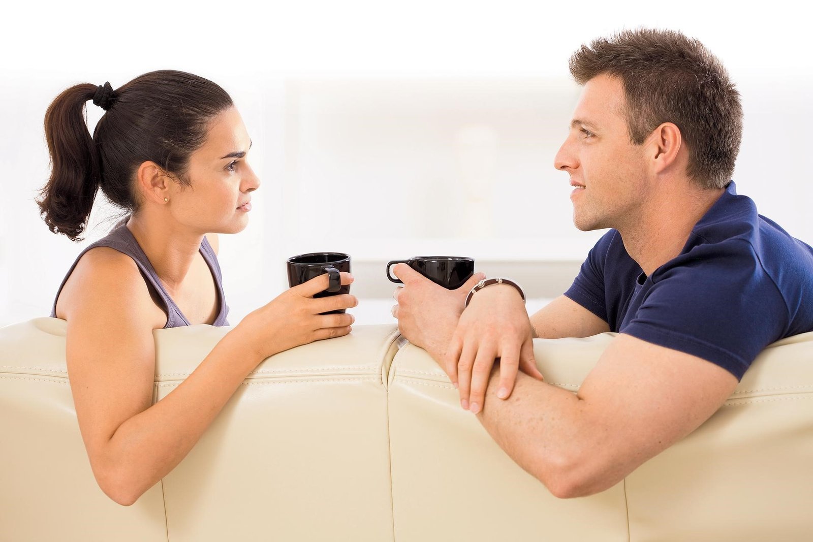 Um casal de frente, sentados em um sofá e tomando uma xícara de café