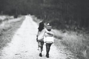 Duas crianças abraçadas e caminhando por uma estrada de terra