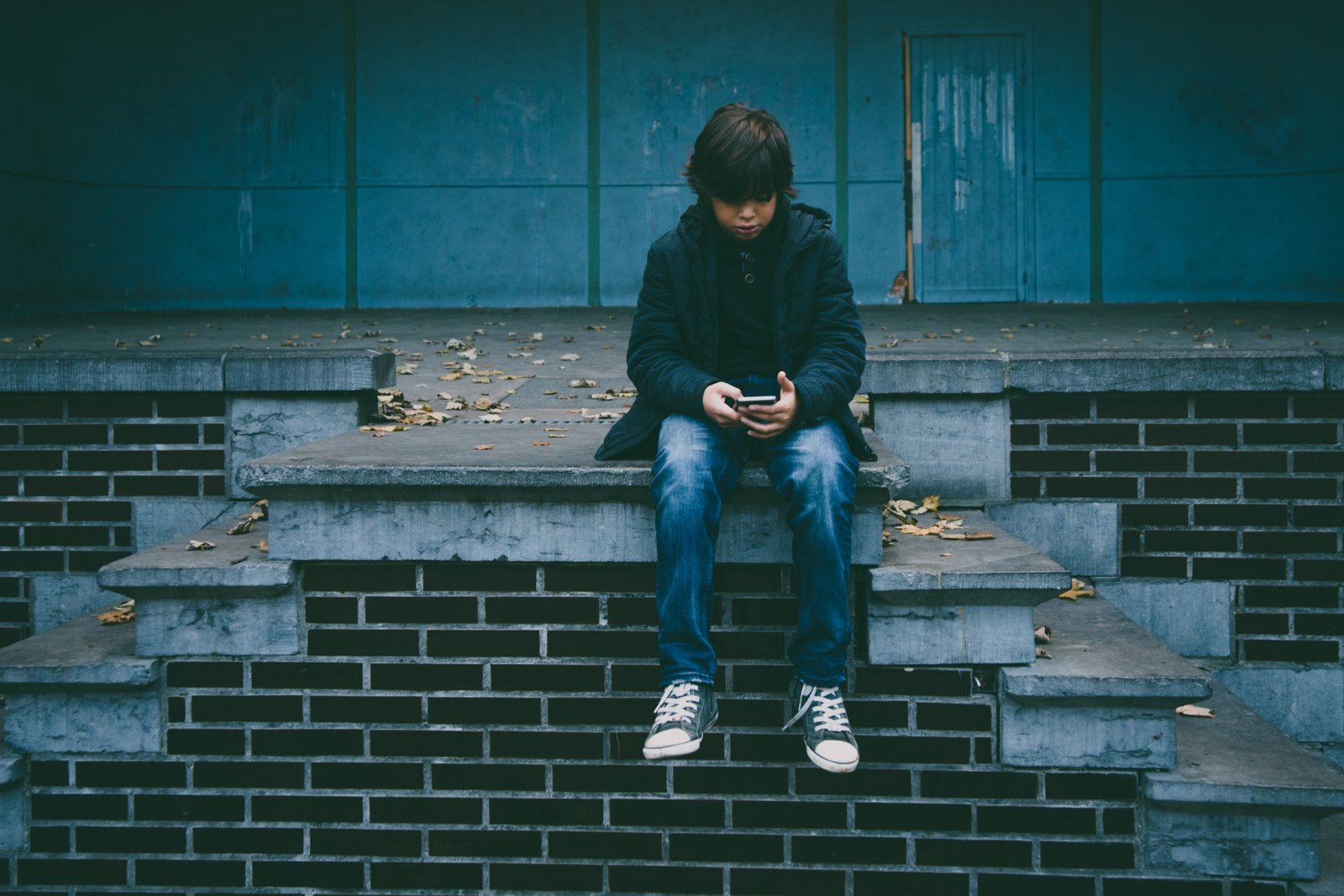 Uma garoto sentado em cima de uma escadaria e olhando para o seu celular