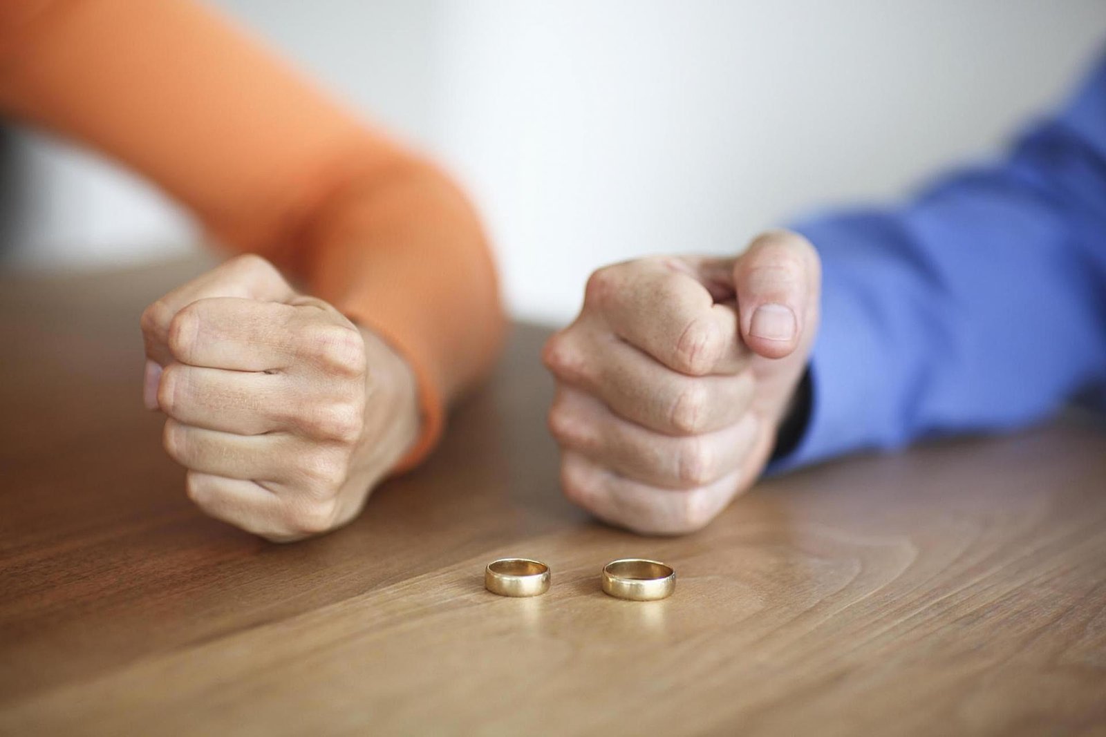Um par de alianças sobre a mesa, enquanto um casal apoia suas mãos fechadas sobre ela