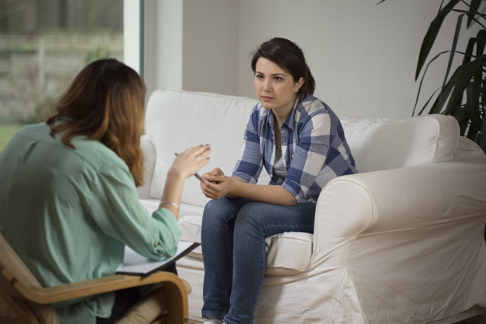 Uma mulher sentada no sofá enquanto ouve sua psicóloga falando