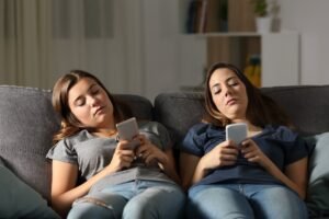Duas mulheres deitadas em um sofá e mexendo em seus smartphones