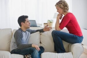 Uma mulher sentada no braço do sofá enquanto fala com seu namorado