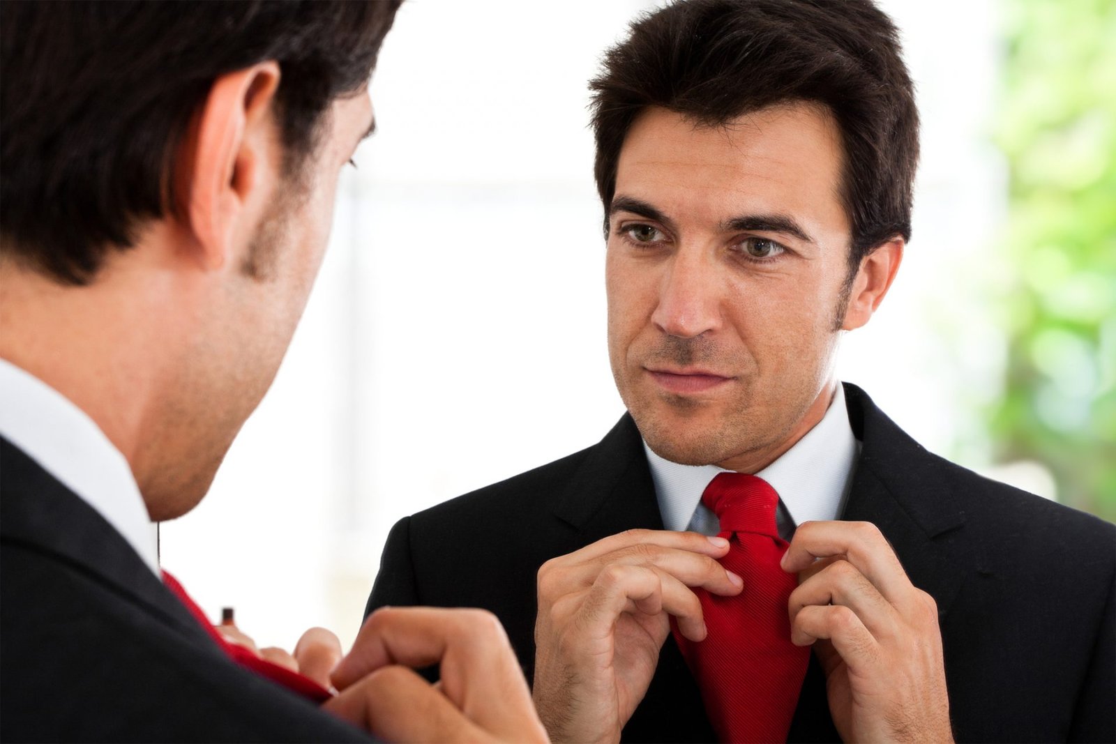 Homem se olhando no espelho enquanto ajeita sua gravata