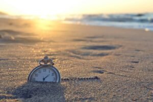 Um relógio semi enterrado na areia da praia