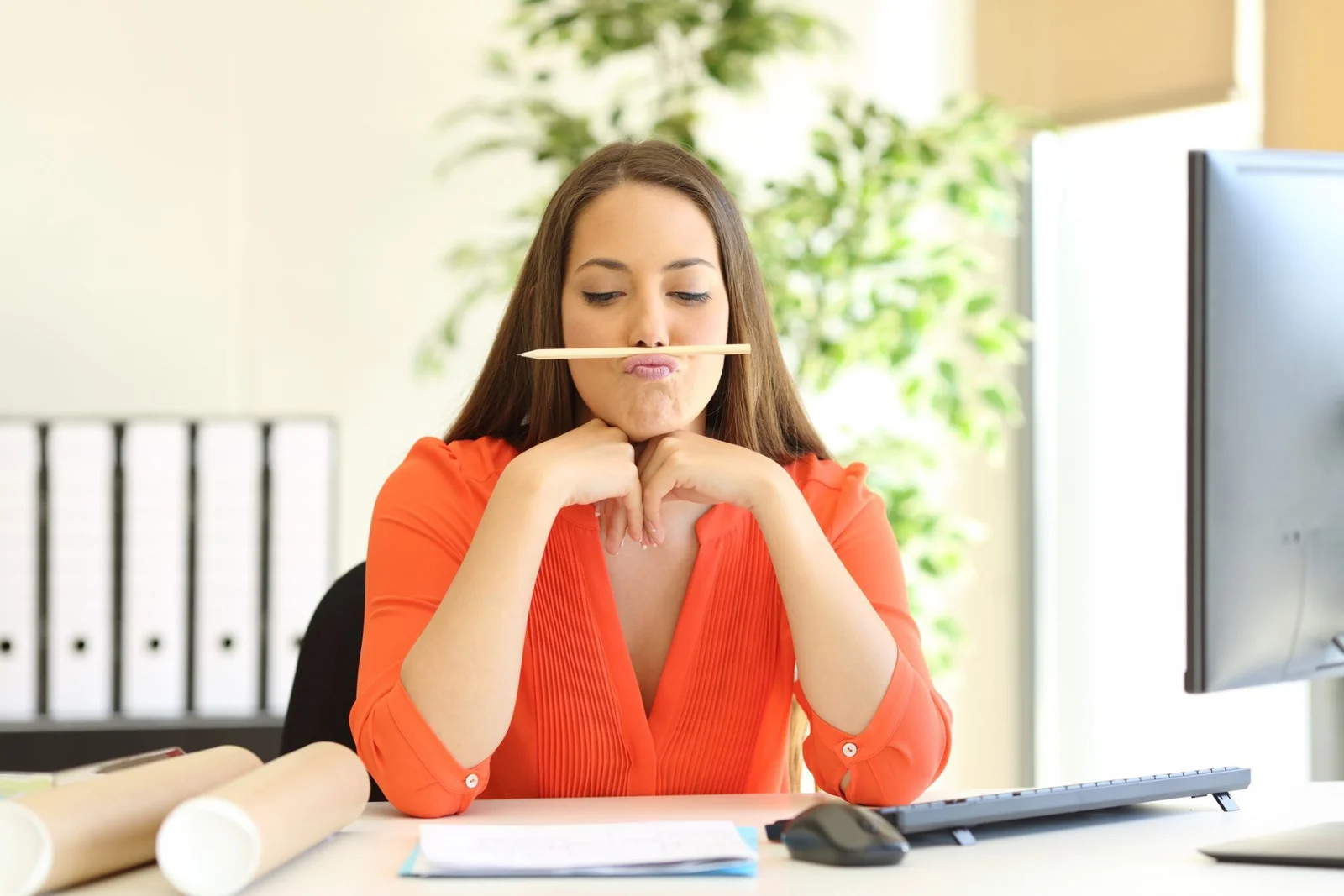 Uma mulher segurando um lápis entre seus lábios e o nariz em um ambiente de trabalho