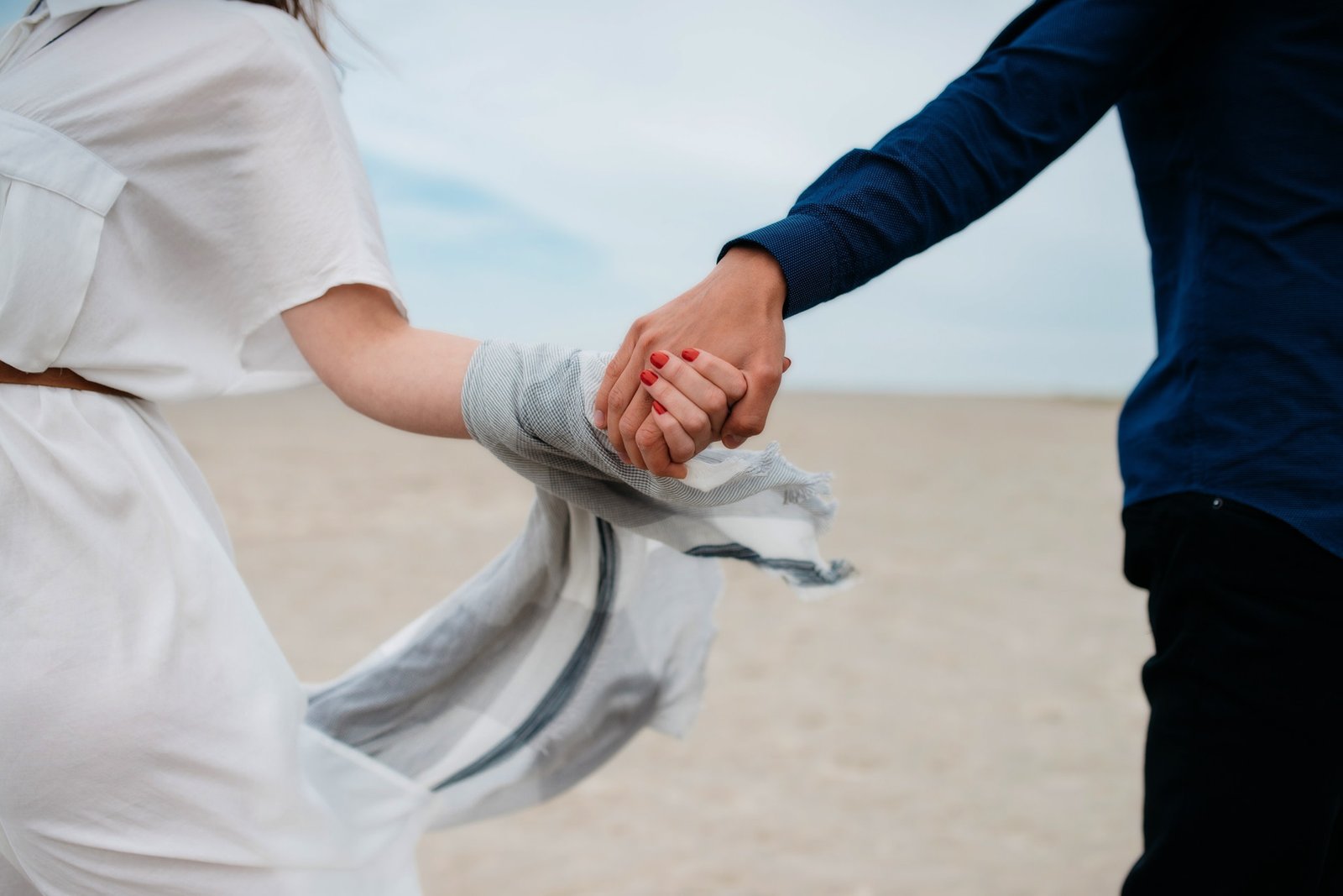 Um casal com as mãos amarradas por um pano enquanto caminham em uma praia