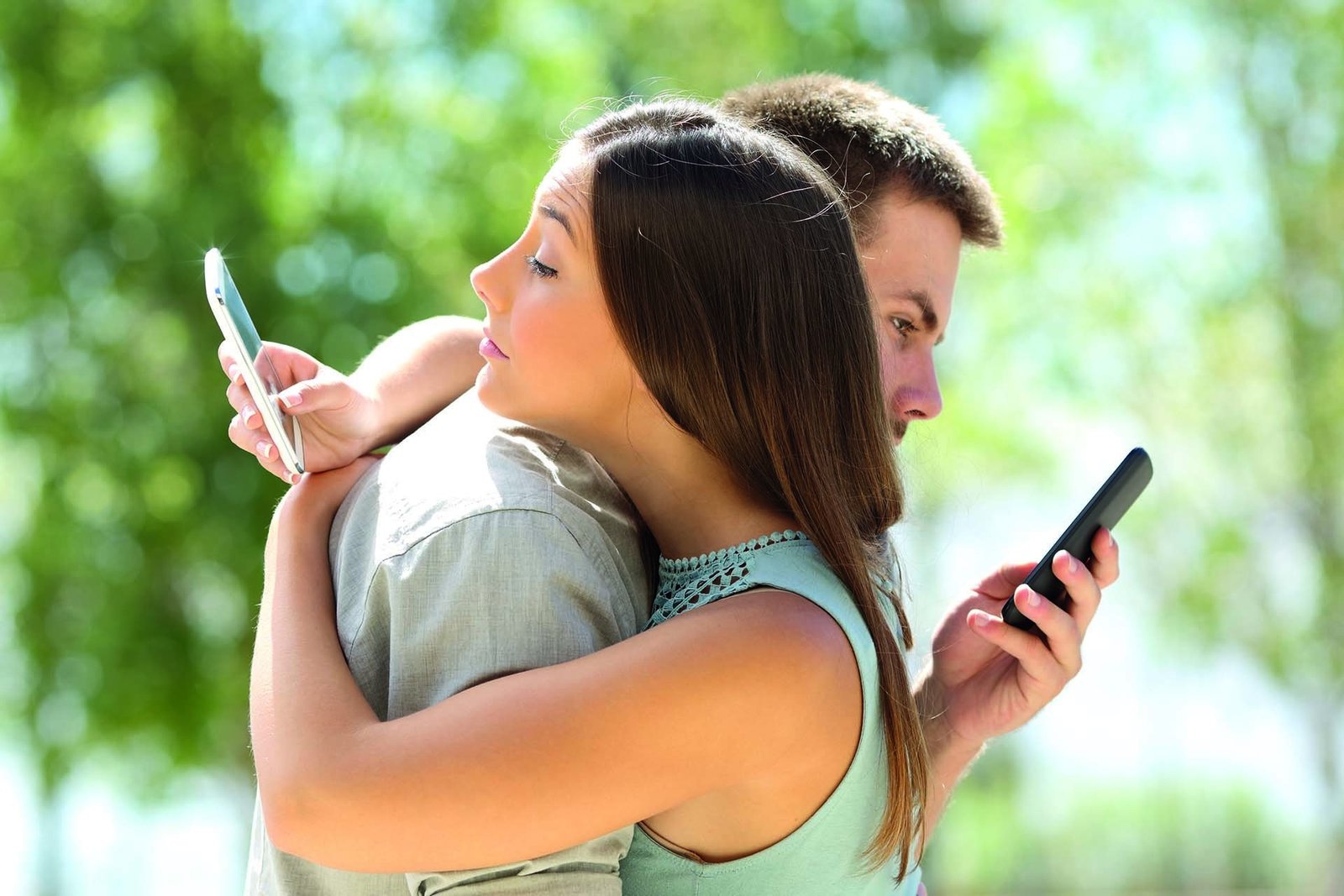 Um casal abraçado enquanto cada um olha para a tela do seu próprio celular