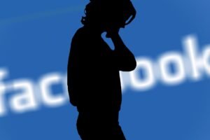 Silhueta de uma mulher, com o logo do Facebook fora de foco ao fundo