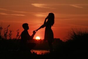 Silhueta de um homem ajoelhado em frente à uma mulher durante o pôr-do-sol