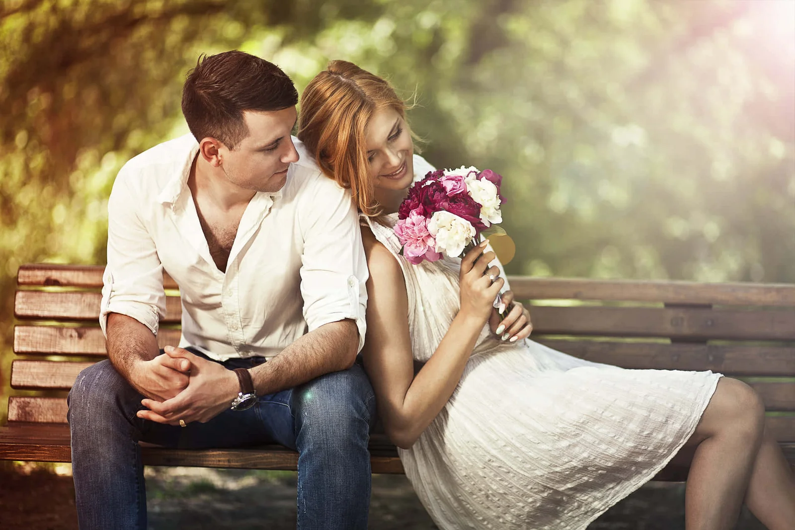 Um casal sentado em um banco de madeira enquanto a mulher segura um buquê de rosas