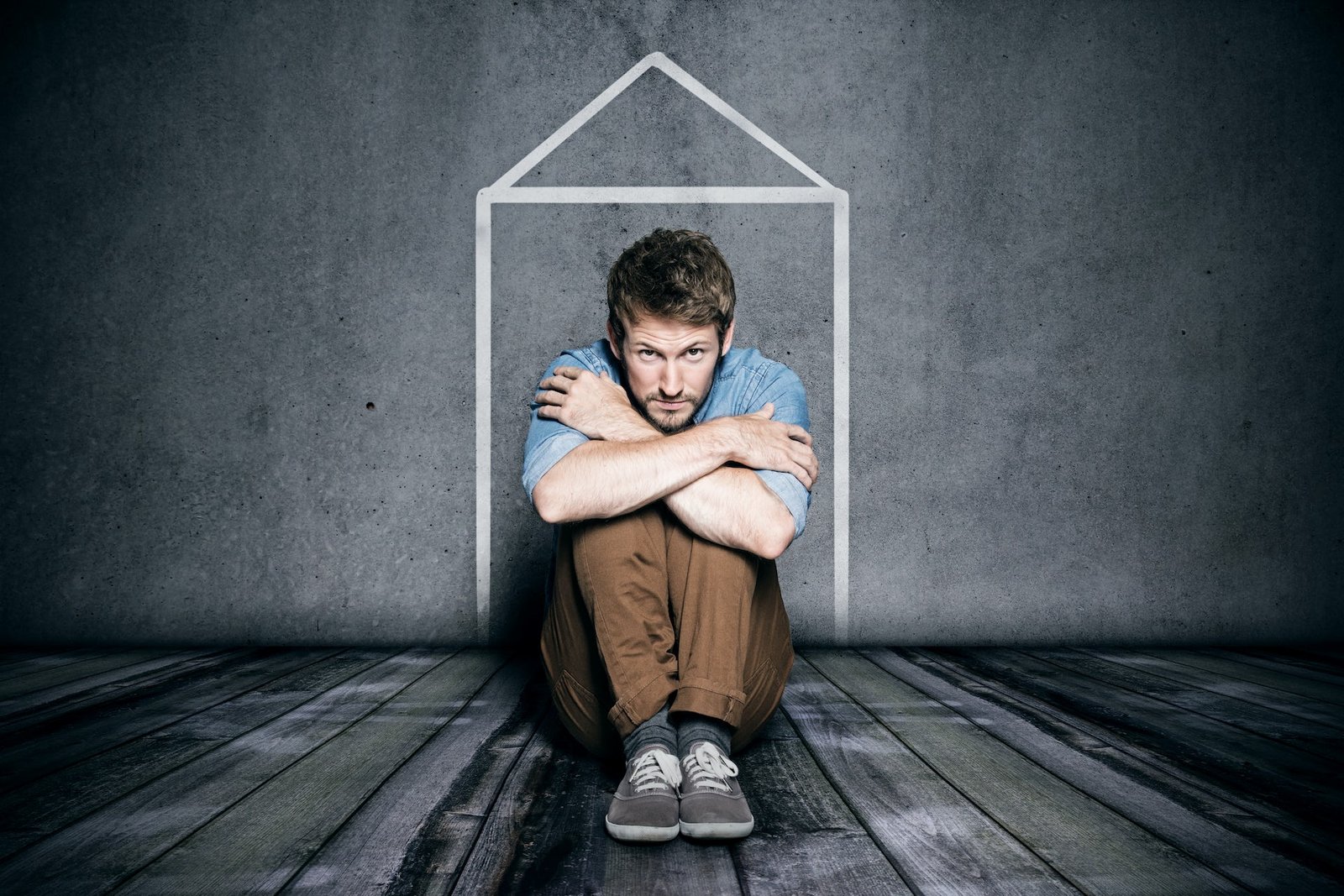Um homem triste e sentado dentro de uma casa desenhada com giz branco