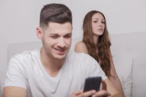 Um homem cometendo uma mcrotraição no celular enquanto sua namorada olha desconfiada